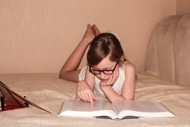 istock A child with glasses is lying on the bed and reading a book. Distance learning. 1346545469