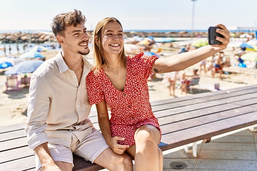 Young hispanic couple on vacation smiling happy standing at the beach