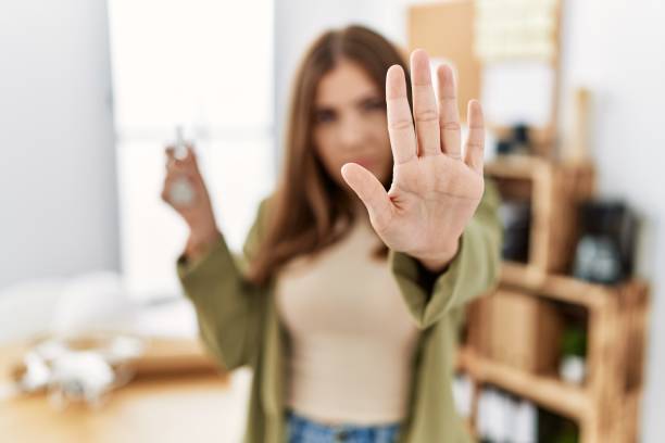 istock Young brunette woman working at architecture office holding house keys with open hand doing stop sign with serious and confident expression, defense gesture 1346547266