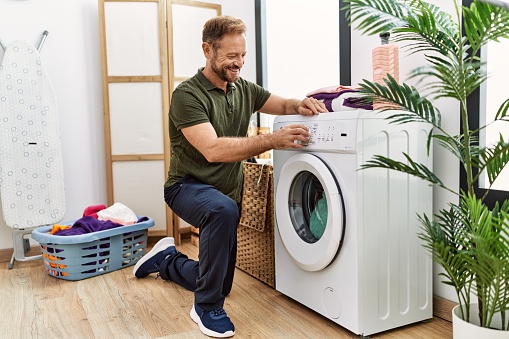 Middle age hispanic man smiling confident washing clothes at laundry room