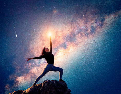 latin woman is dancing or posing on the top of the mountain pointing to the sky and the Milky Way background