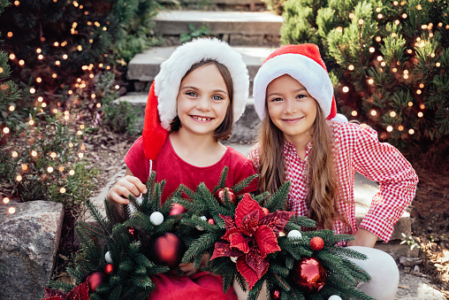 Merry Christmas. Portrait of two happy funny children girls in Santa hat with Christmas wreath. Happy Holidays. Fairy Magic. Happy kids enjoying holiday.