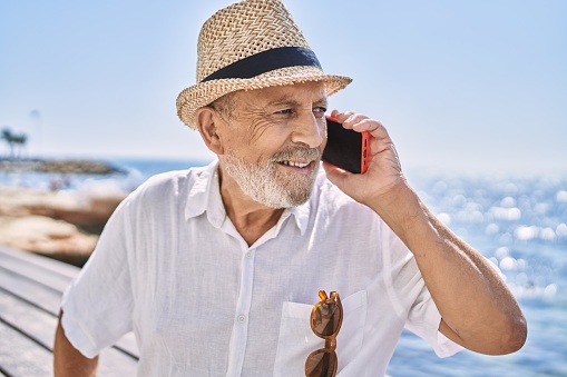 Senior man wearing summer hat talking on the smartphone at seaside