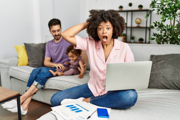 집에서 컴퓨터 노트북을 사용하여 일하는 인종 간 가족의 어머니는 머리에 손을 가지고 무서워하고 입을 벌리고 충격을 두려워하고 놀랐습니다. - surprise shouting child black and white 뉴스 사진 이미지