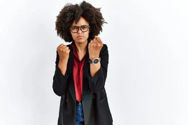 Photo of African american woman with afro hair wearing business jacket and glasses ready to fight with fist defense gesture, angry and upset face, afraid of problem