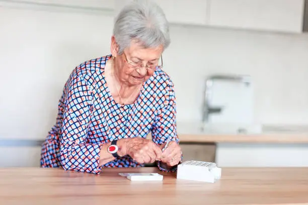 Old woman with emergency alarm button putting pills into pill box. Medical care concept