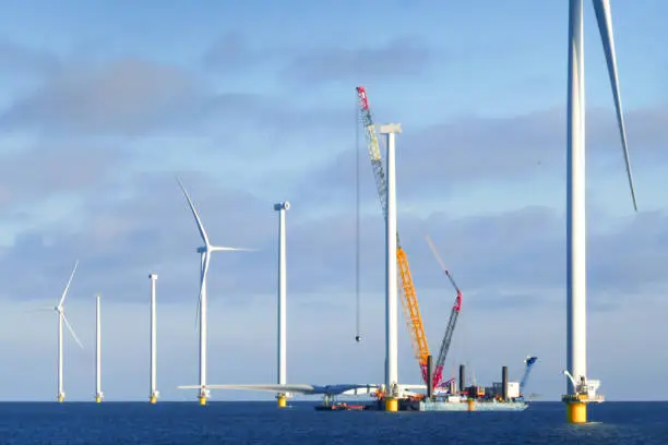 Photo of Construction of offshore wind farm - wind turbine in Netherland on the sea (markermeer). Crane ship is preparing for lifting up rotor of the wind turbine. Sunny weather and atmospheric mood.