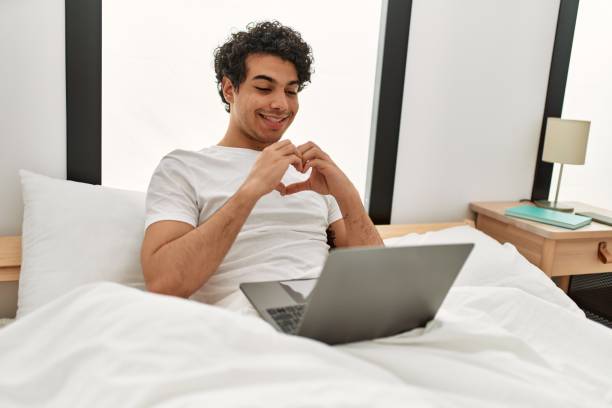 istock Young hispanic man having video call doing heart symbol with hands at bedroom. 1346554179