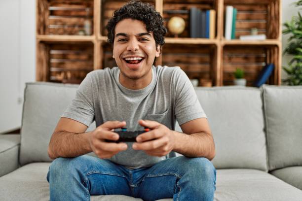 istock Young hispanic man playing video game sitting on the sofa at home. 1346554205