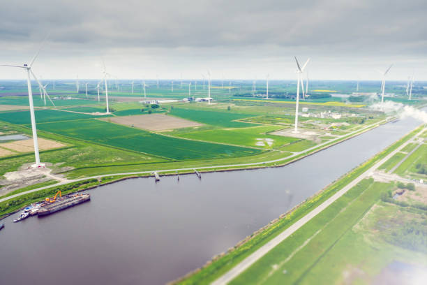 View on wind farm in Netherland around canal. Fields, roads and industrial river ship (barge) under wind turbines. Cloudy weather.