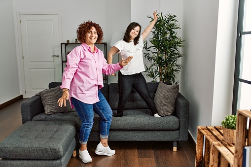 Mature mother and down syndrome daughter at home dancing on the sofa