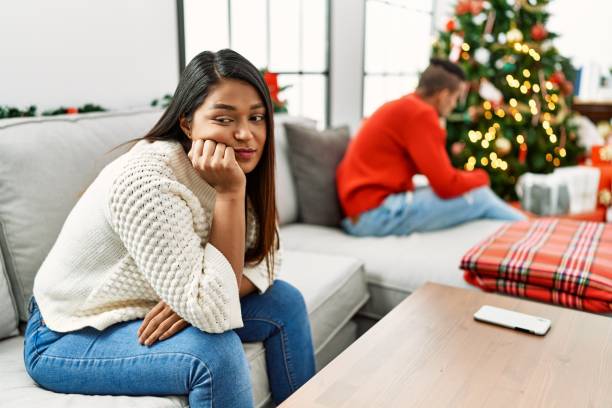 giovane coppia latina su problemi con espressione triste seduta sul divano di casa. - holiday emotional stress christmas santa claus foto e immagini stock