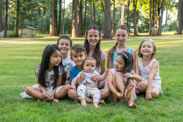 retrato de un grupo multiétnico de niños sentados en la hierba afuera - cousin fotografías e imágenes de stock