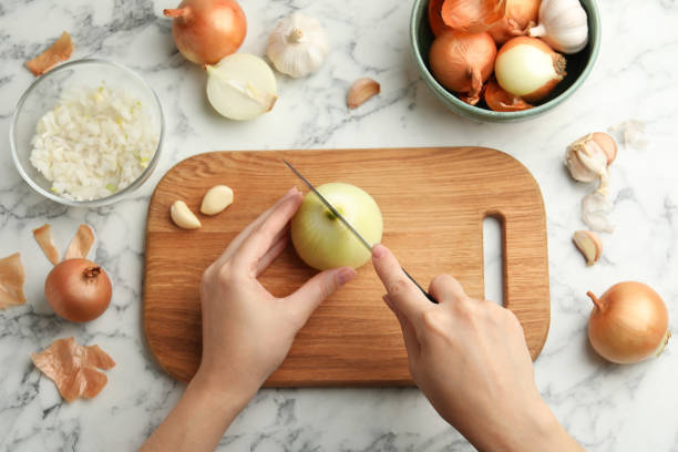 woman cutting fresh onion on wooden board at white marble table, top view - kesmek stok fotoğraflar ve resimler