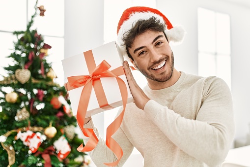 Young hispanic man smiling happy holding gift at home.
