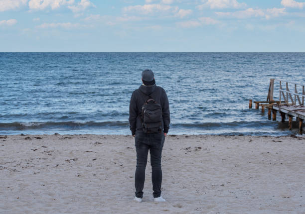 rear view of man wearing hooded sweater and jeans looking at the sea