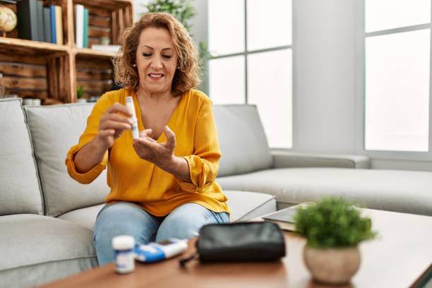 donna caucasica di mezza età che misura il glucosio seduta sul divano di casa. - diabetes foto e immagini stock