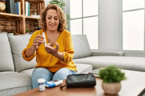 Middle age caucasian woman measuring glucose sitting on the sofa at home.