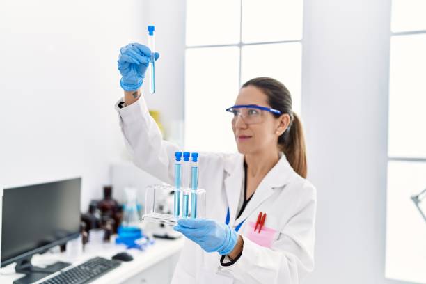 Young hispanic woman wearing scientist uniform holding test tube at laboratory stock photo