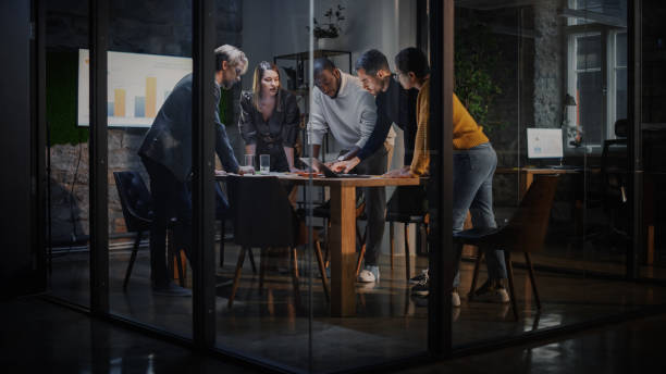 young creative team meeting with business partners in conference room behind glass walls in agency. colleagues sit behind conference table and discuss business opportunities, growth and development. - 解決辨法 個照片及圖片檔