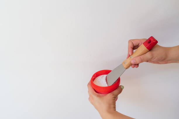 흰색 배경에 주걱으로 퍼티 벽을 들고 있는 여성. 퍼티 나이프가 흰 페이스트를 얼룩지게 하는 인간의 손 - plasterboard plaster repairing putty 뉴스 사진 이미지