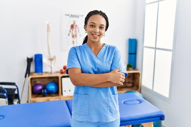 giovane donna afroamericana che lavora alla clinica di recupero del dolore faccia felice sorridente con le braccia incrociate guardando la telecamera. persona positiva. - male smiling african descent black foto e immagini stock