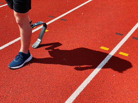 A close-up low section shot of an unrecognizable teenage male athlete with a prosthetic leg walking across a running track outdoors.