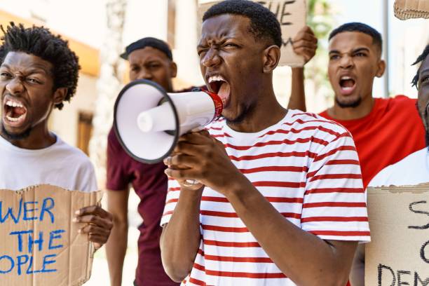 istock Group of young african american activists protesting holding banner and using megaphone at the city. 1346567359