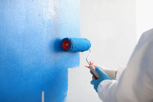 istock Repairman painting white wall in apartment blue using roller closeup 1346567463