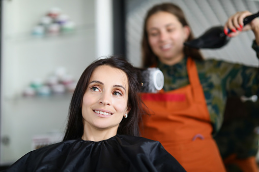 Woman hairdresser drying and straightening client hair with brushing and hairdryer. Hair care concept