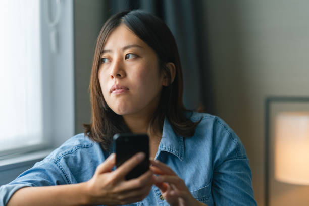 istock Young woman sitting on sofa by window and using smart phone st home 1346568766