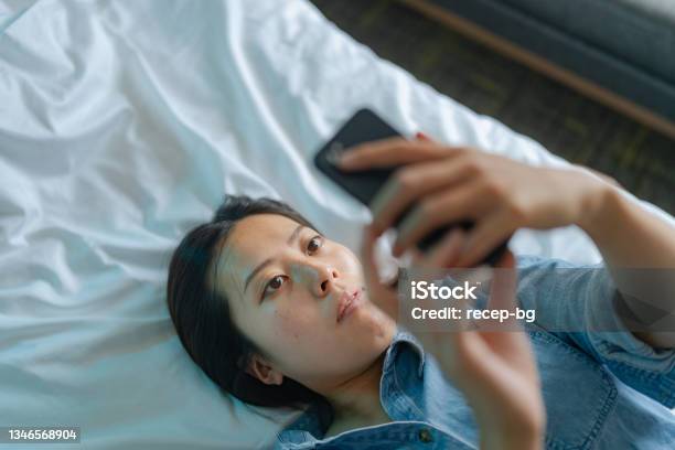 High Angle View Of Young Woman Using Smart Phone While Lying Down On Her Bed Stock Photo - Download Image Now