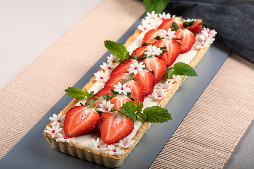 Cake with panna cotta cream and strawberries, decorated with mint and white marzipan flower.