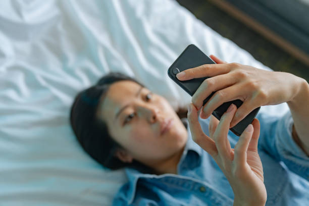 istock High angle view of young woman using smart phone while lying down on her bed 1346569282