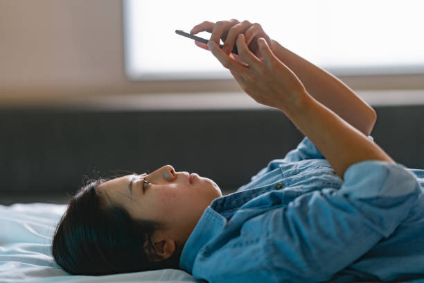 jeune femme allongée sur son lit et utilisant un téléphone intelligent - telephone window mobile phone addiction photos et images de collection