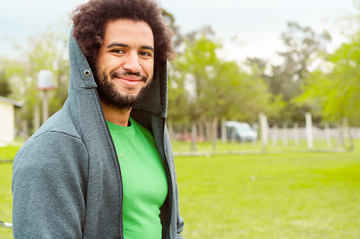 Portrait of smiling male environmentalist. Confident mid adult man is standing in park. He is wearing hooded jacket.