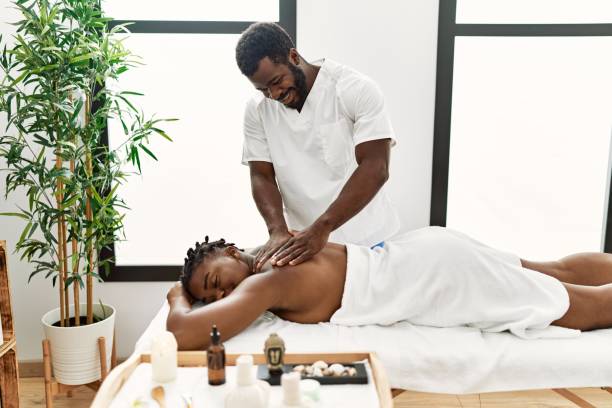 Young physiotherapist man smiling happy giving back massage to african american woman at the clinic. Young physiotherapist man smiling happy giving back massage to african american woman at the clinic. black male massage stock pictures, royalty-free photos & images