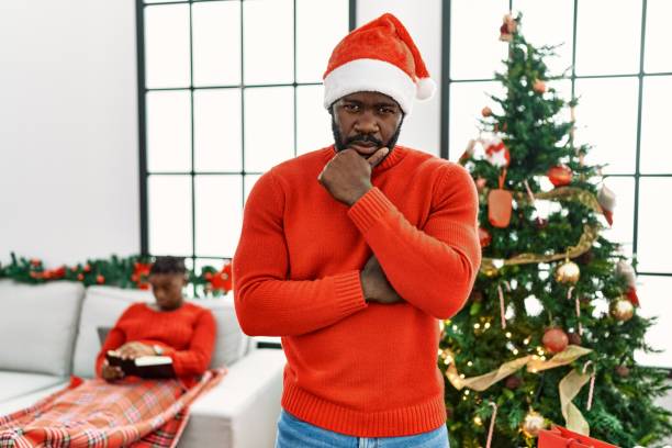 istock Young african american man standing by christmas tree looking confident at the camera smiling with crossed arms and hand raised on chin. thinking positive. 1346573155
