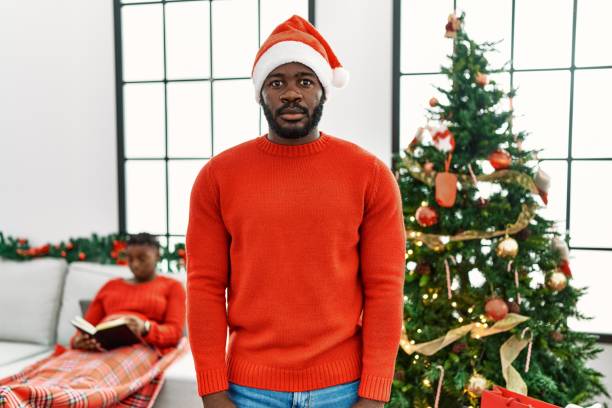 istock Young african american man standing by christmas tree relaxed with serious expression on face. simple and natural looking at the camera. 1346573186