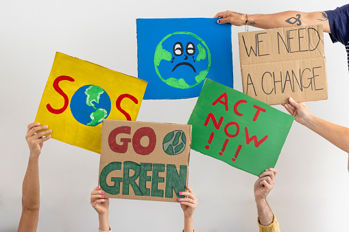 A group of unrecognisable people holding placards with environmental messages on them against a white background. They are protesting for climate change.