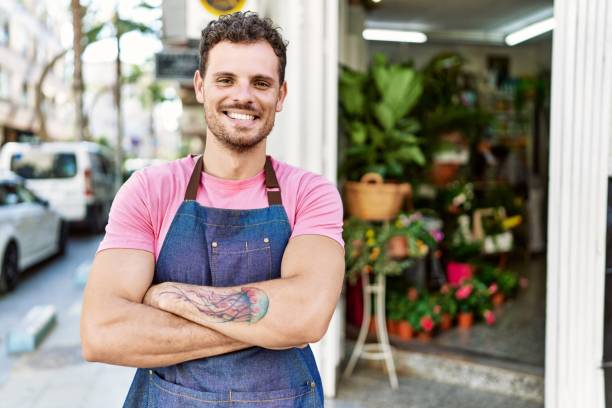 Young hispanic worker wearing apron standing with arms crossed gesture at the florist. stock photo