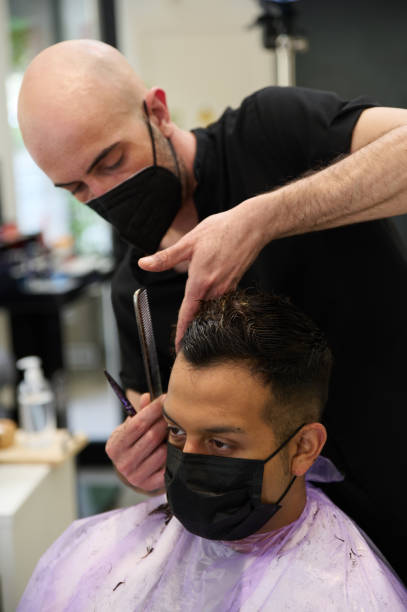 istock Barber cutting costumer hair with scissors wearing mask 1346576413