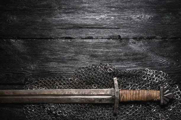 Knight sword and chain mail on the black wooden table flat lay background with copy space.