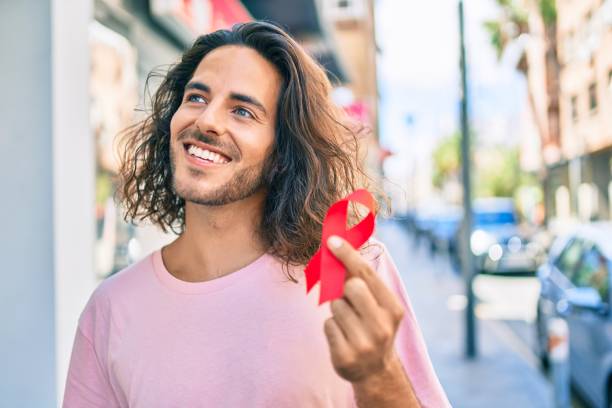 Young hispanic man smiling happy holding hiv awareness red ribbon at city. Young hispanic man smiling happy holding hiv awareness red ribbon at city. town of hope stock pictures, royalty-free photos & images
