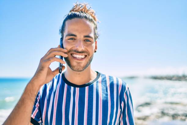 istock Young hispanic man smiling happy talking on the smartphone at the beach. 1346578102