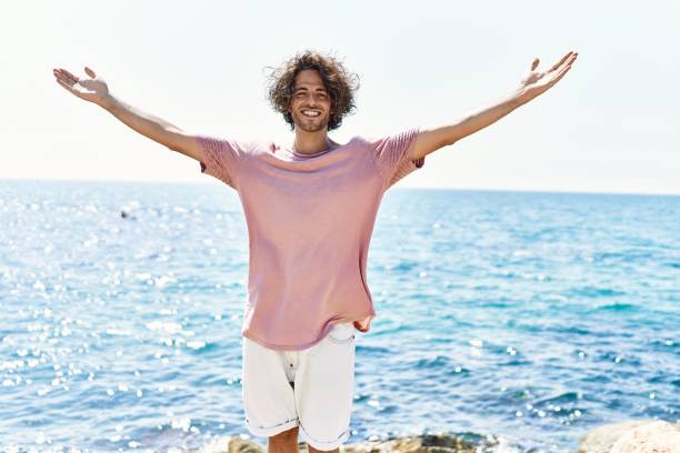 istock Young hispanic man breathing standing with arms open at the beach. 1346578152