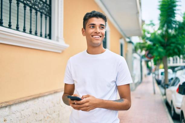 Young latin man smiling happy using smartphone walking at the city. stock photo
