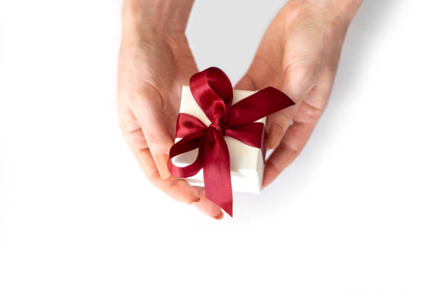 istock Female hands hold white box with red bow on white background. Gift box in female hands 1346578772