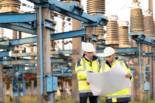 istock Engineers in special clothing are working on site. Two engineers discuss a drawing on paper in the open air against the background of a high-voltage power line 1346580181