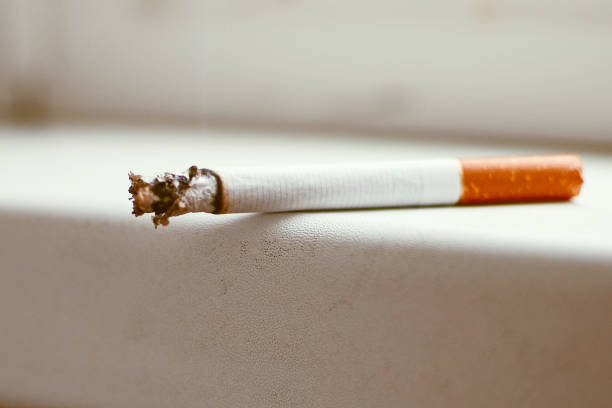 istock a white cigarette with a yellow filter smoulders smokes lying on the windowsill on the window 1346580250